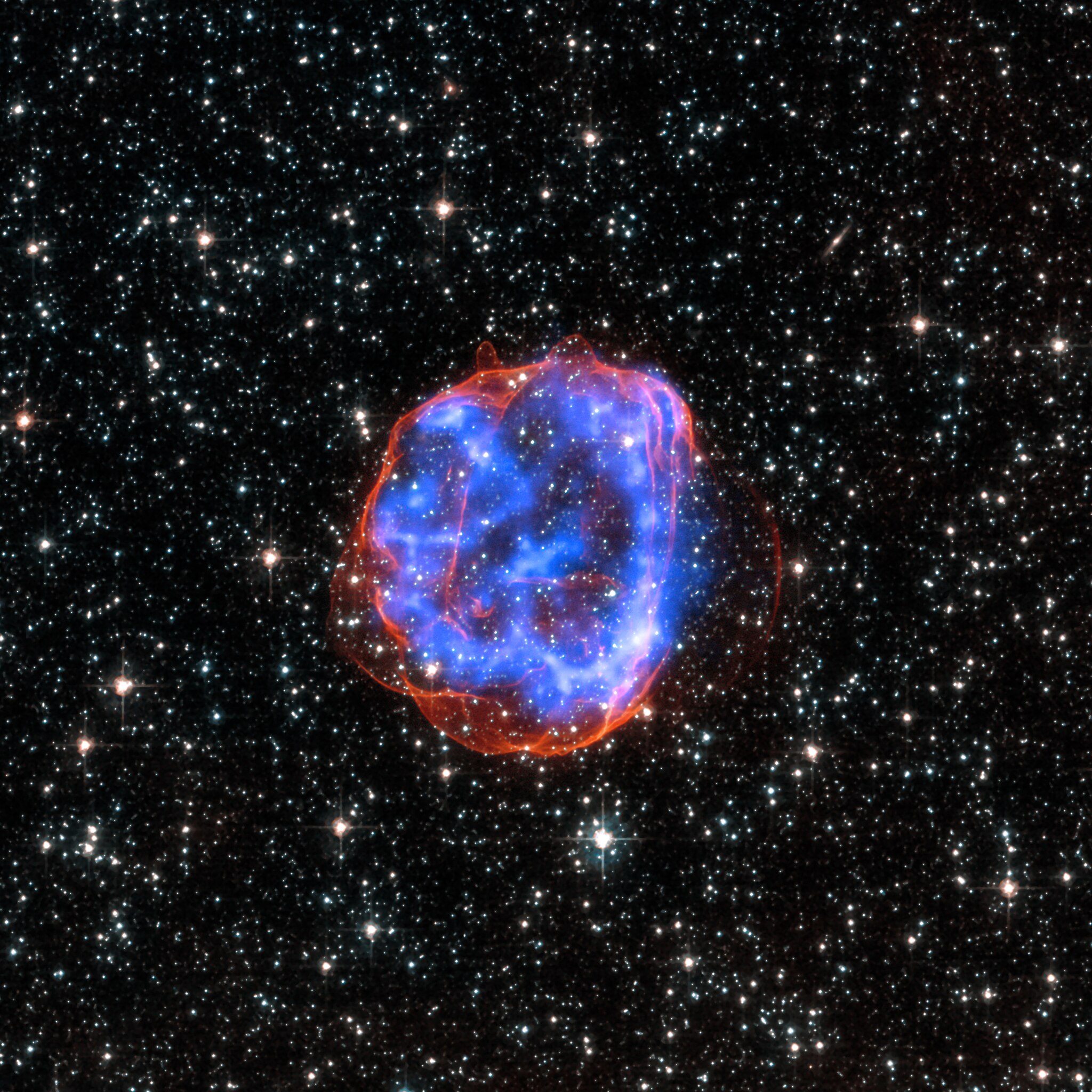 X-ray & Optical Images of SNR E0519-69.0 - When a massive star exploded in the Large Magellanic Cloud, a satellite galaxy to the Milky Way, it left behind an expanding shell of debris called SNR 0519-69.0. Here, multimillion degree gas is seen in X-rays from Chandra (blue). The outer edge of the explosion (red) and stars in the field of view are seen in visible light from Hubble.