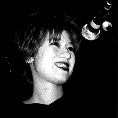 Miki Berenyi, chanteuse de Lush, au micro sur scène, photographie noir et blanc grenée prise depuis la fosse, vers 1990