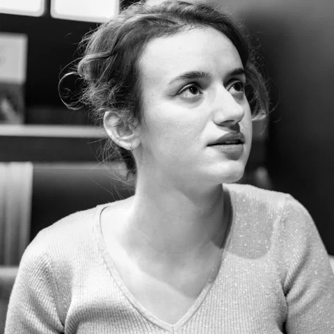 Portrait en noir et blanc de la romancière Perrine Tripier, de trois quarts, cheveux relevés, le regard porté hors-champ vers le haut, les lèvres entrouvertes, à l'écoute ; lumière douce, fond sombre.