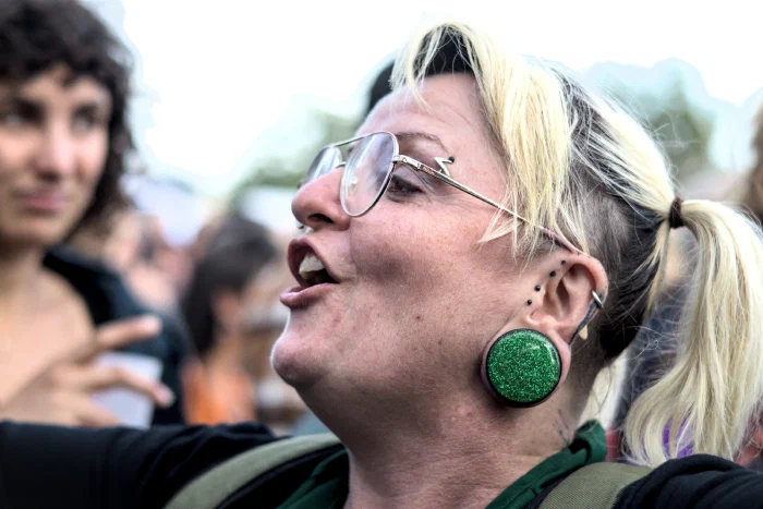 Blonde festival-goer in aviator glasses and a green glitter ear plug singing along, Binic Folk Blues Festival 2025