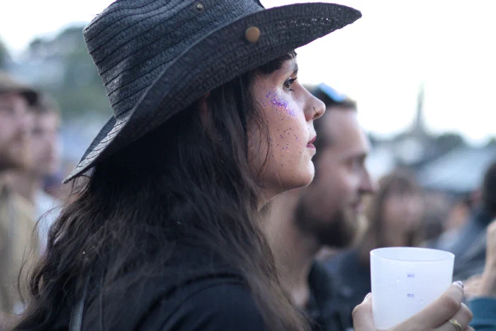 Woman in a black hat with purple glitter across her cheekbone, in profile, Binic Folk Blues Festival 2025