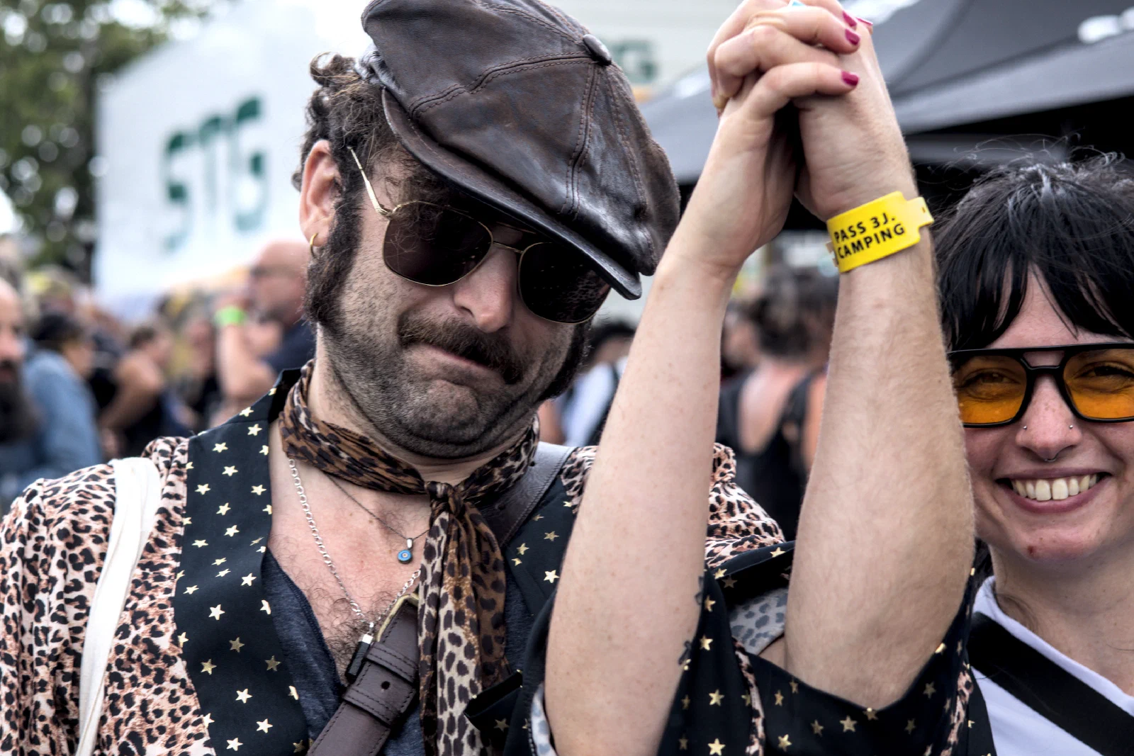 A couple with clasped hands raised in the air, the man in a flat cap and star-print vest, the woman in orange-tinted glasses, Binic Folk Blues Festival 2025