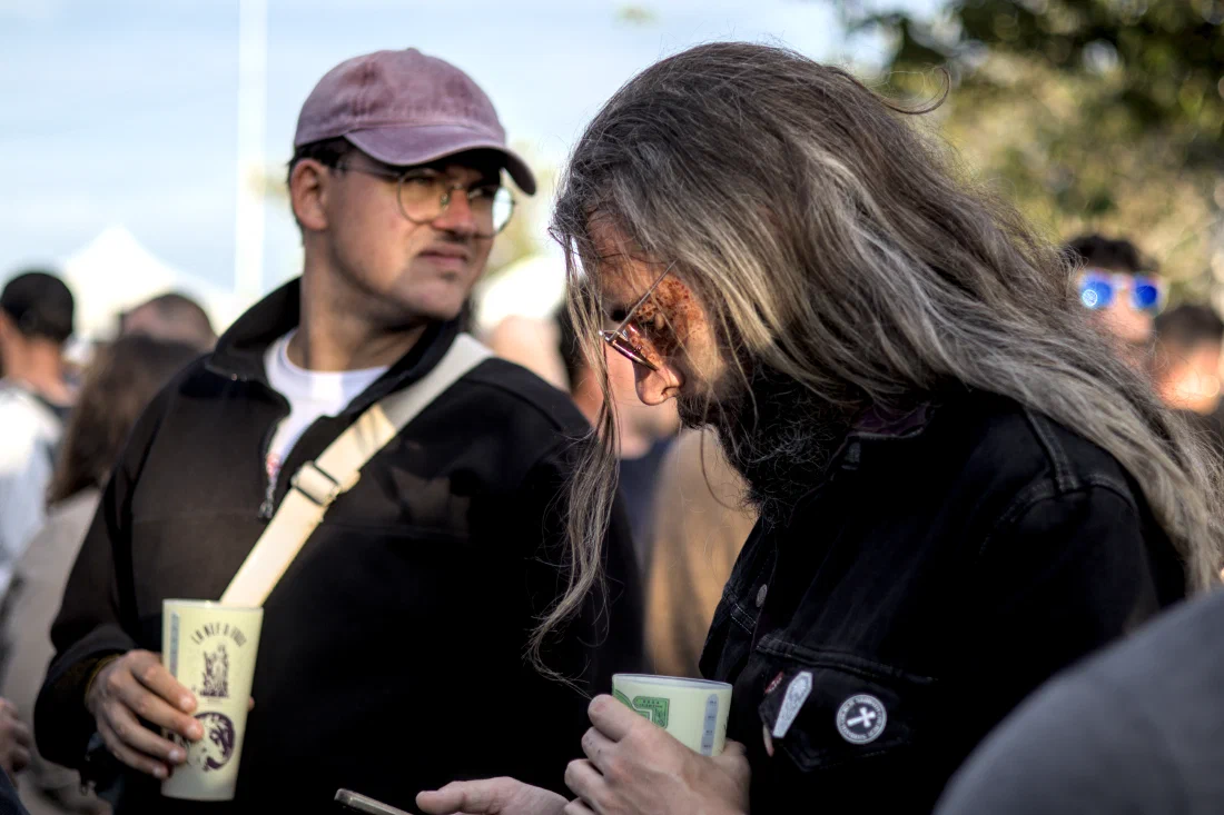 Long grey-haired festival-goer with red glitter around one eye and a pin-covered denim jacket, holding a cup, Binic Folk Blues Festival 2024