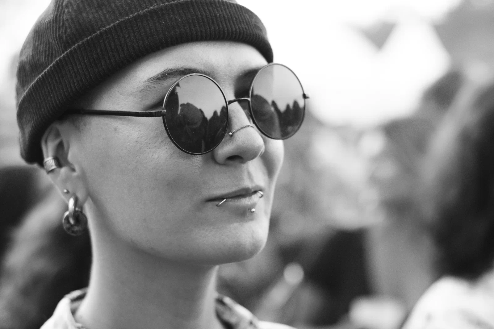 Black-and-white close-up of a festival-goer in a beanie and round mirrored sunglasses reflecting the crowd, Binic Folk Blues Festival 2026